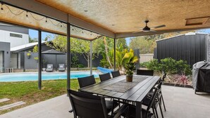 An outdoor patio with a pool, a table and chairs, and a ceiling fan.