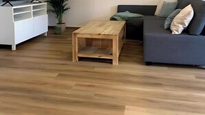 Un salon doté d’un plancher en bois, d’un meuble de rangement blanc pour appareils électroniques, d’un canapé de couleur foncée agrémenté de coussins et d’une petite table basse en bois.