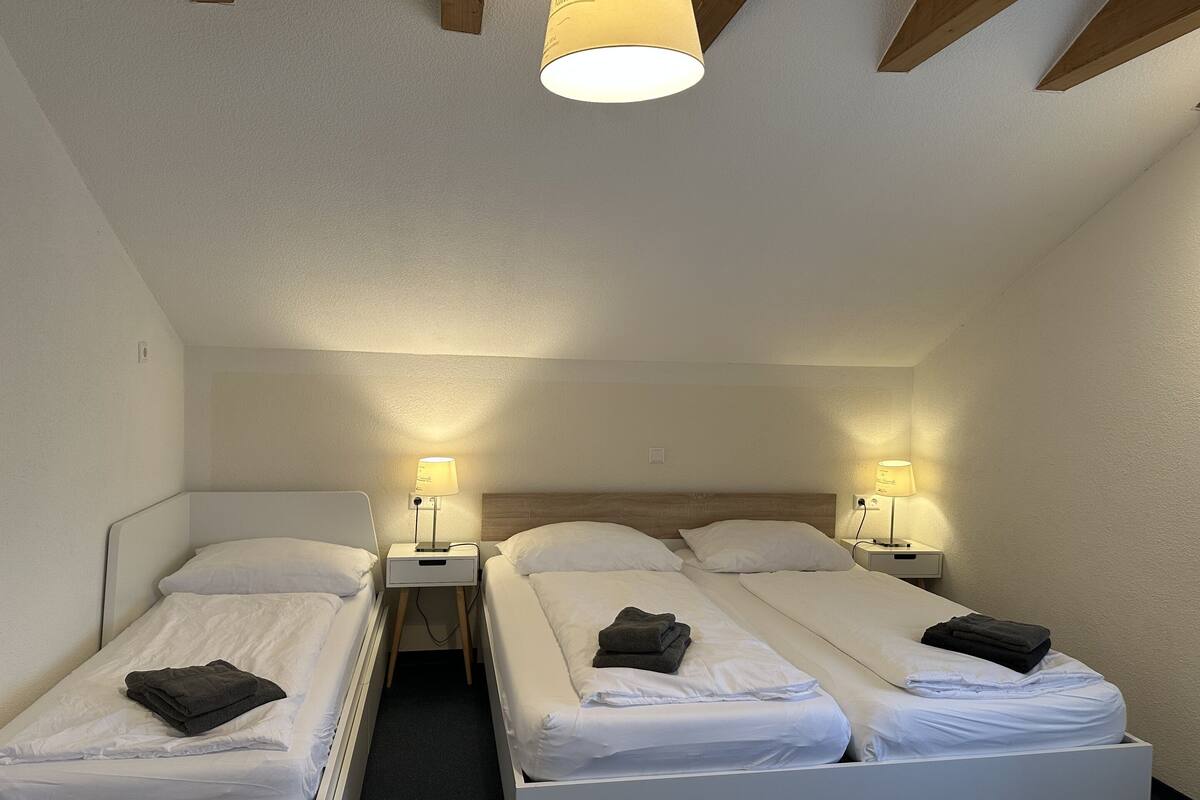 A hotel room with two single beds, each with a bedside table and lamp, and a ceiling light fixture.