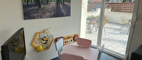 Habitación con un cuadro de un bosque, zona de juegos para niños, televisión y vista del patio exterior.