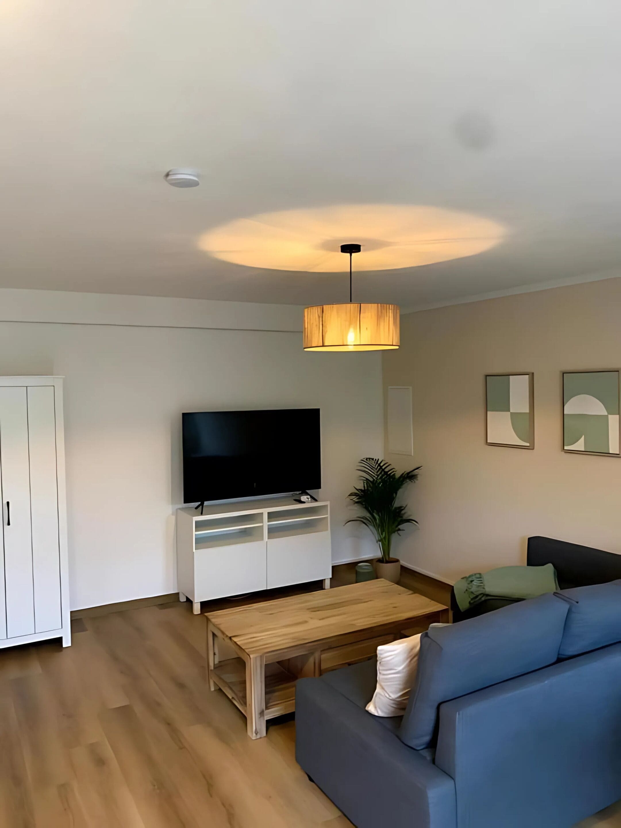 A modern living room with a flat-screen TV, a wooden coffee table, a blue sofa, and a hanging lamp.