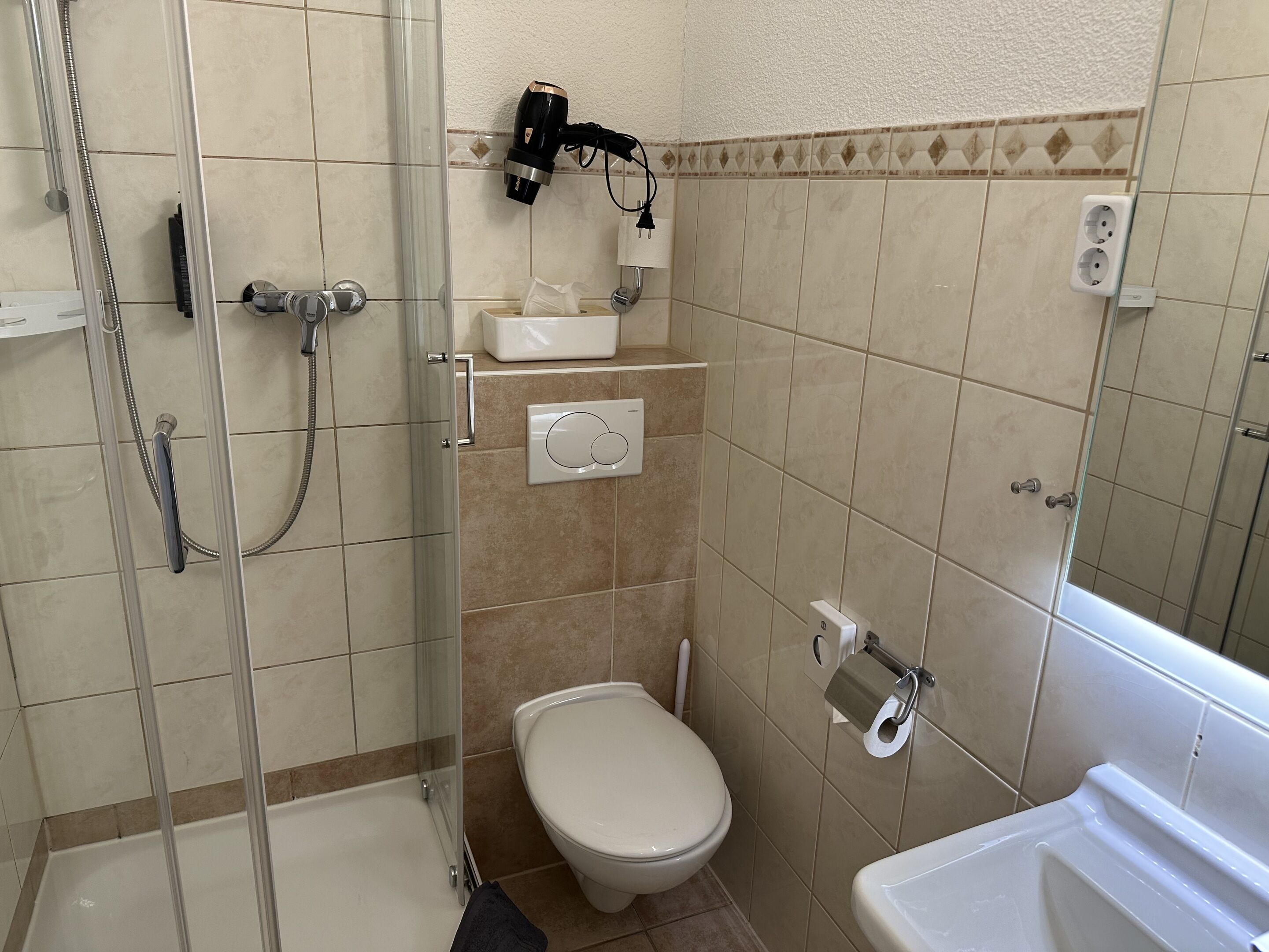A bathroom with a glass-enclosed shower, a toilet, a sink, and a hairdryer mounted on the wall.