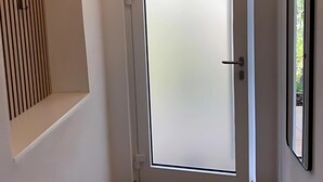 Un couloir avec une porte en verre dépoli, un mur recouvert de lambris en bois et un miroir encadré sur le côté droit.