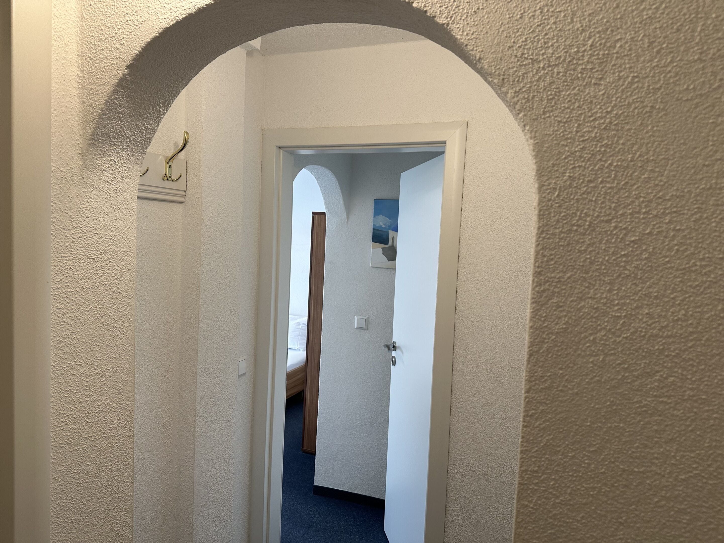 A hallway with a textured white wall, an arched doorway, and a painting on the wall.