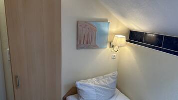Un dormitorio con puerta de madera, una cama con ropa de cama blanca, una lámpara de pared y un cuadro.