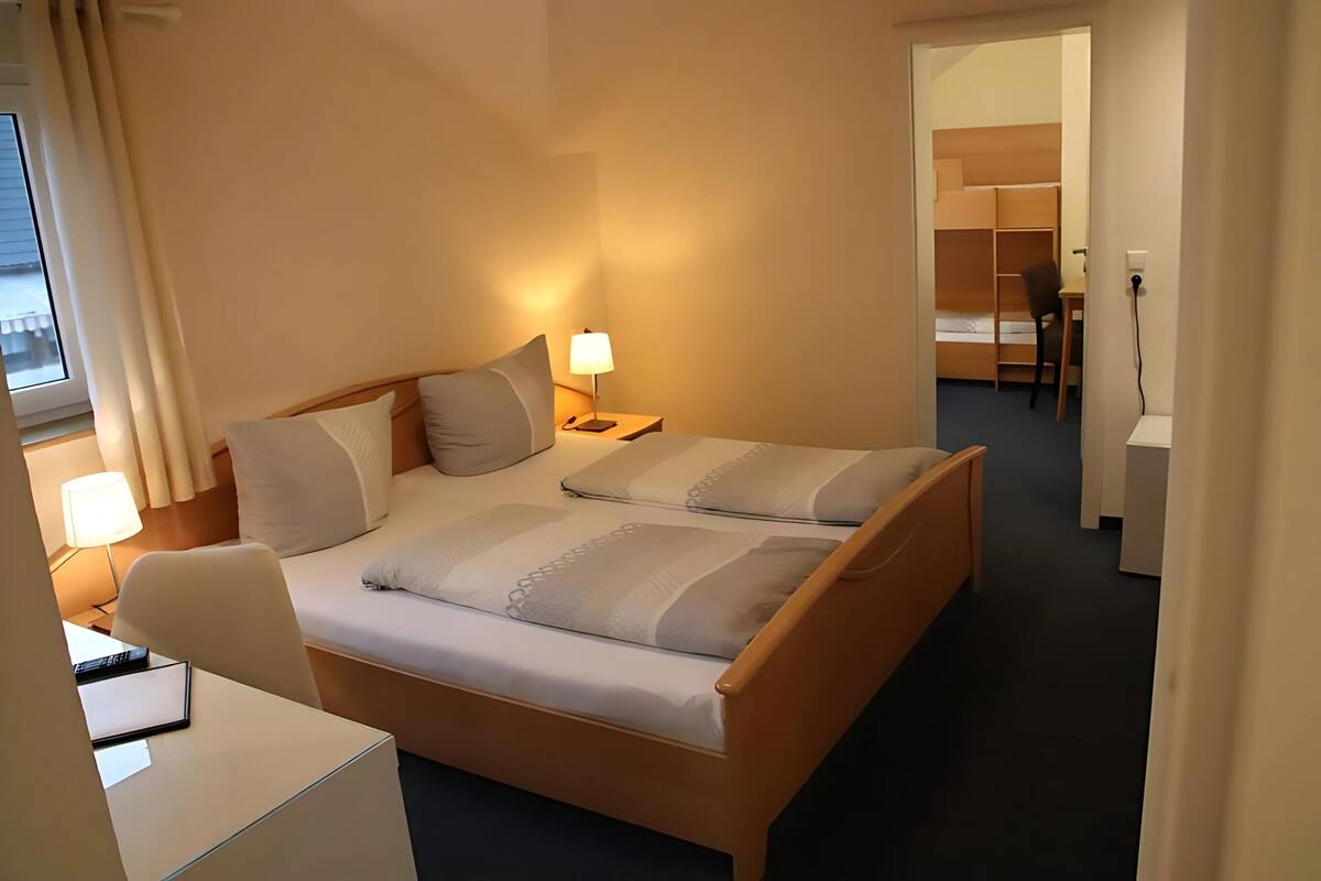 A hotel room with a bed, bedside tables, a desk, and a chair.