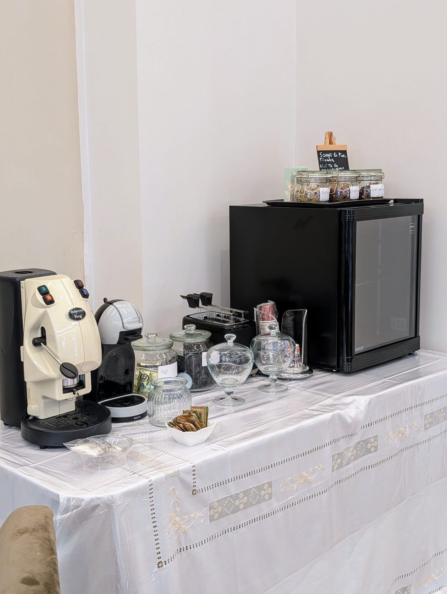 Une petite cuisine équipée d’une machine à café, d’un réfrigérateur et de différents récipients pour conserver les aliments.