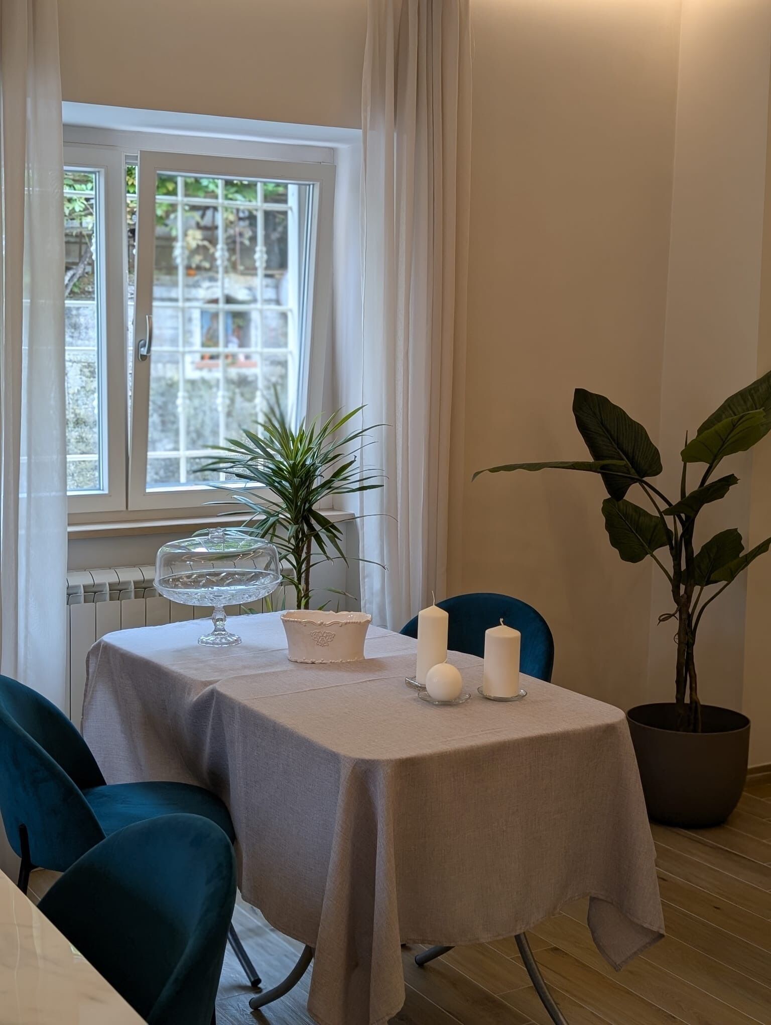 Un comedor con una mesa preparada para dos personas, una planta en maceta y una ventana con cortinas.