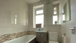 Un baño con bañera, inodoro, tocador y ventana.