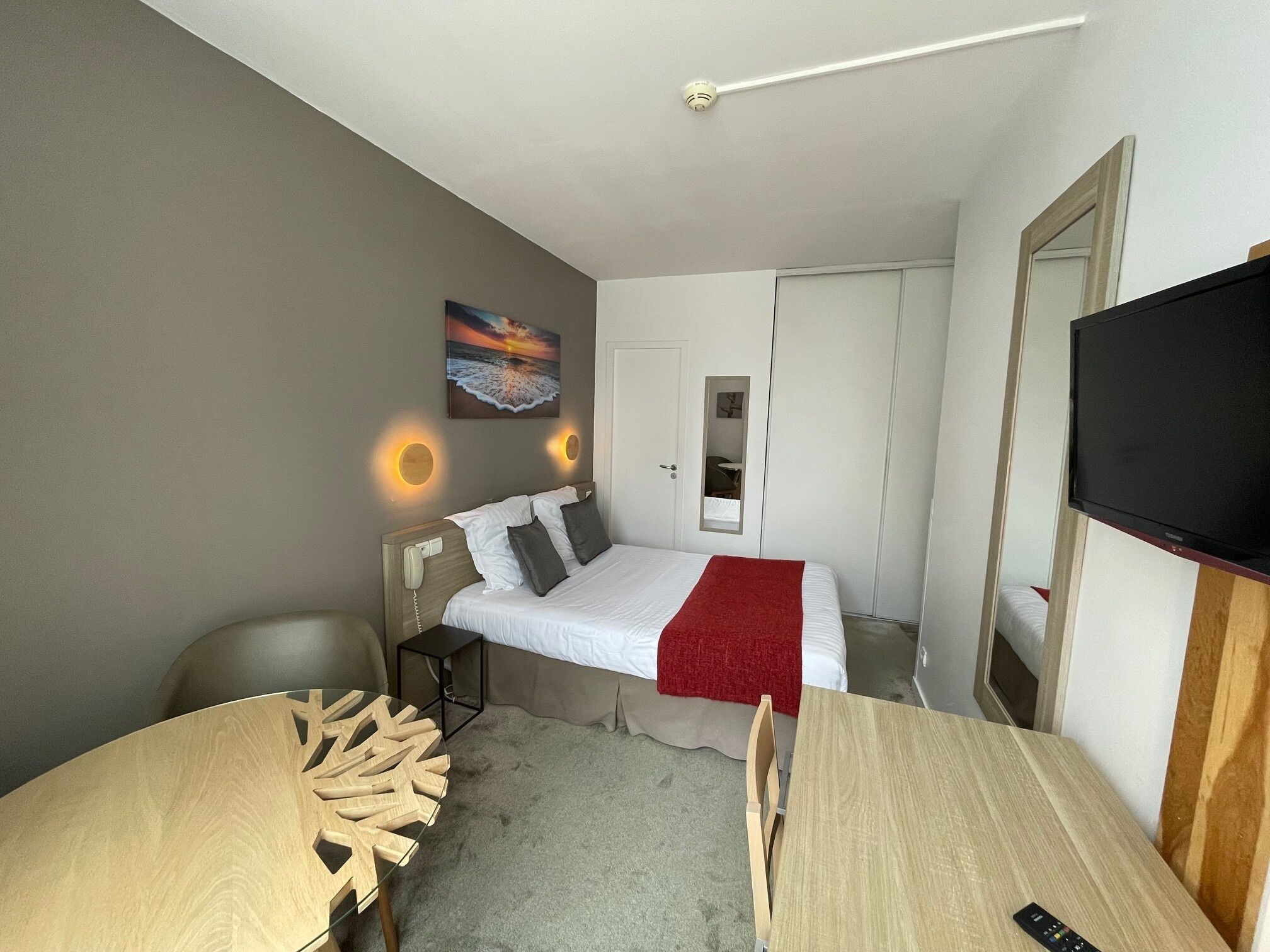 A compact hotel room with a single bed, a desk, a chair, a TV, and a painting on the wall.
