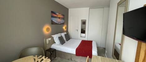 A compact hotel room with a single bed, a desk, a chair, a TV, and a painting on the wall.