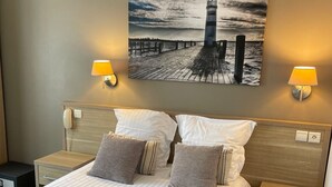 A neatly made bed with striped pillows, two bedside lamps, and a painting of a pier and lighthouse on the wall. - Adonis Cottage La Baule (La Baule-Escoublac)
