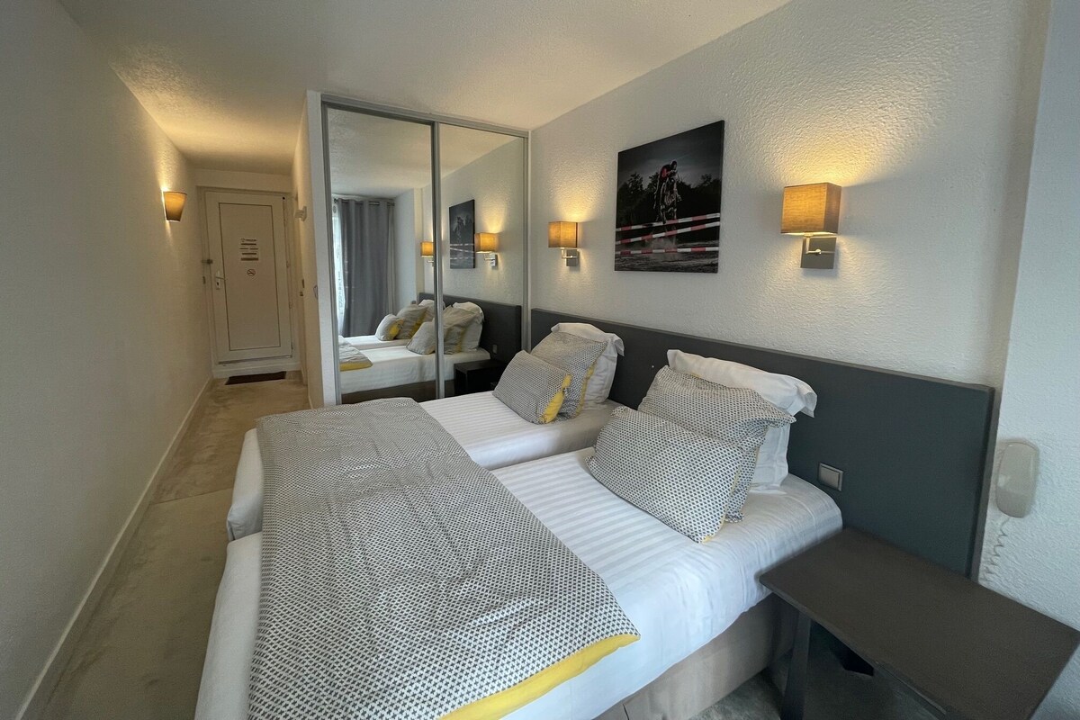 Ein Hotelzimmer mit zwei Betten, einem großen Spiegel, Wandleuchten und einer Tür.