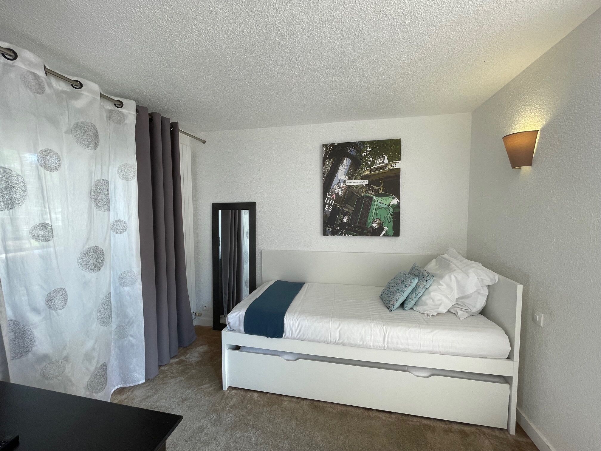 A bedroom with a bed, a bedside table, a wall-mounted artwork, and a window with curtains.