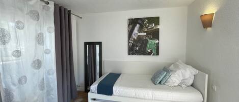A bedroom with a bed, a bedside table, a wall-mounted artwork, and a window with curtains.