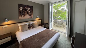 A modern hotel room with a large bed, a painting on the wall, a balcony with outdoor furniture, and a view of greenery outside. - Adonis Cottage La Baule (La Baule-Escoublac)