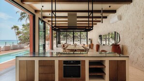 Une cuisine moderne dotée d’un four encastré, un coin repas avec une grande table et une vue sur l’océan.