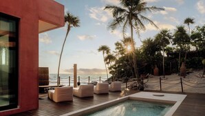 Een modern zwembadgedeelte met ligbedden, een houten terras en uitzicht op de oceaan en palmbomen.