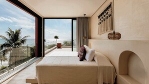 Een slaapkamer met een groot bed, uitzicht op de oceaan en een balkon met een palmboom.