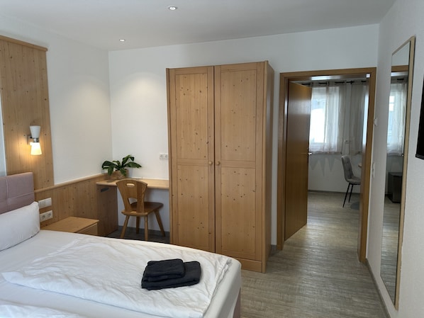 A bedroom with a bed, a wooden wardrobe, a desk with a chair, and a potted plant. - Gästehaus Ludwig (Rust)