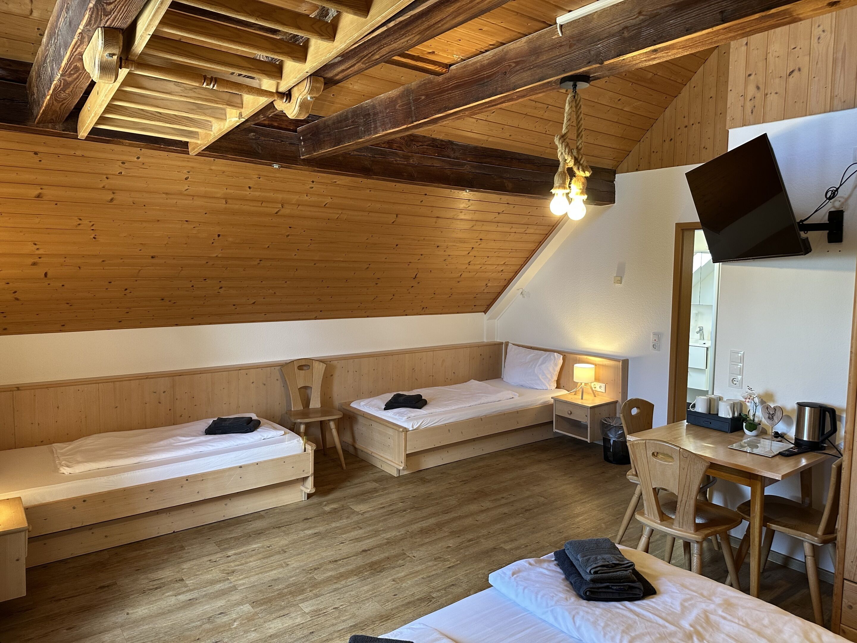 A room with two wooden bunk beds, a desk with a chair, a television mounted on the wall, and a wooden ceiling.