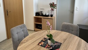 Ein Zimmer mit einem runden Holztisch, zwei gestreiften Stühlen, einer kleinen Holzablage mit einer Pflanze, einem Toaster und einem Wasserkocher.