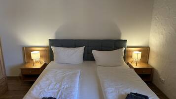 A double bed with two pillows, two bedside tables with lamps, and folded towels on the bed.