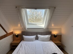 A bedroom with a skylight, two bedside tables, a bed with white bedding, and a view of trees outside. - Gästehaus Ludwig (Rust)