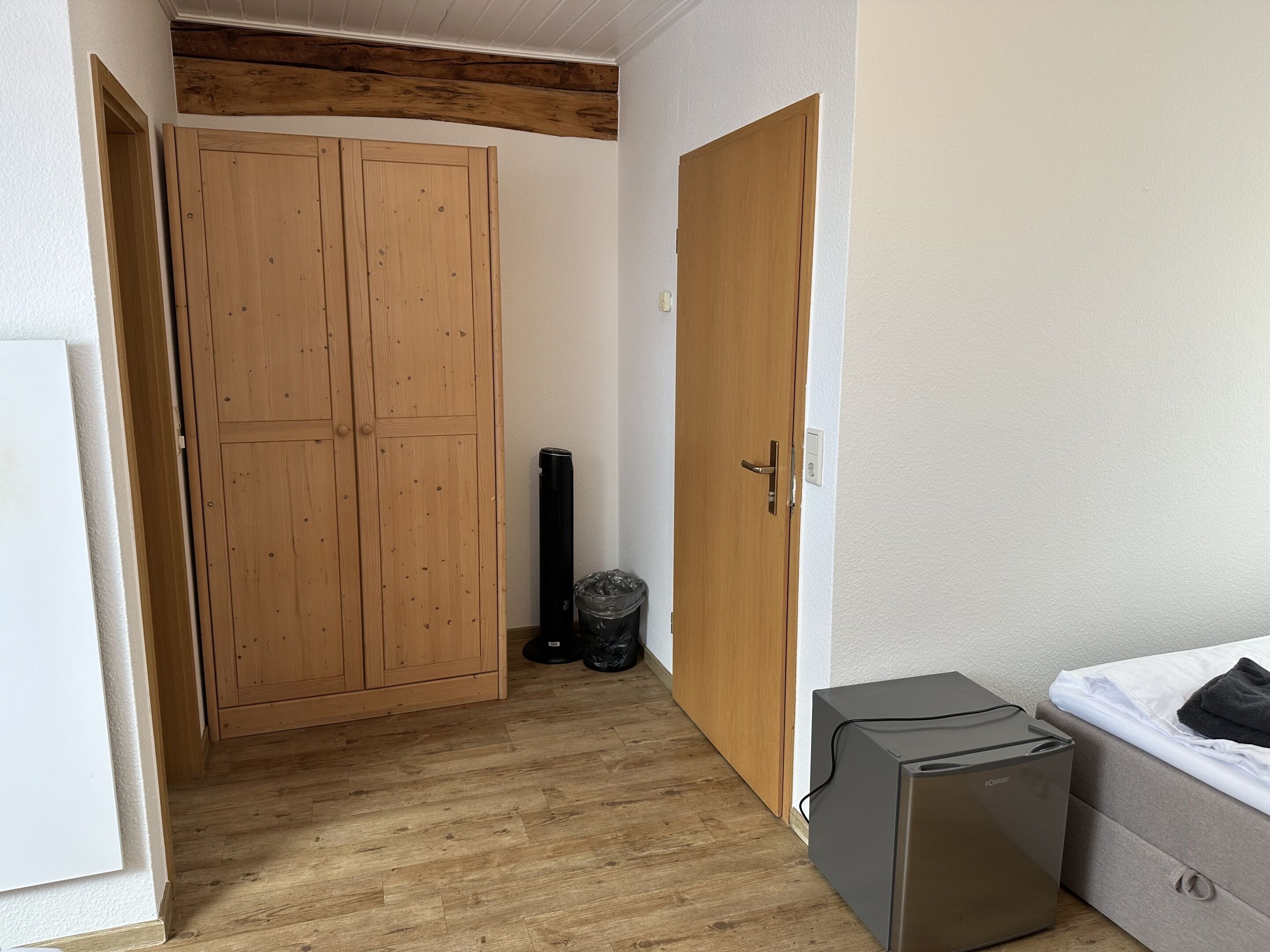 Ein Zimmer mit einem Holzschrank, einem kleinen grauen Gerät und einem Bett mit weißer Matratze.