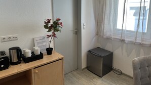 Eine Küchenzeile mit Kaffeemaschine, Tassen, einem Blumentopf, einem kleinen Kühlschrank und einer Tür mit einem Schild.