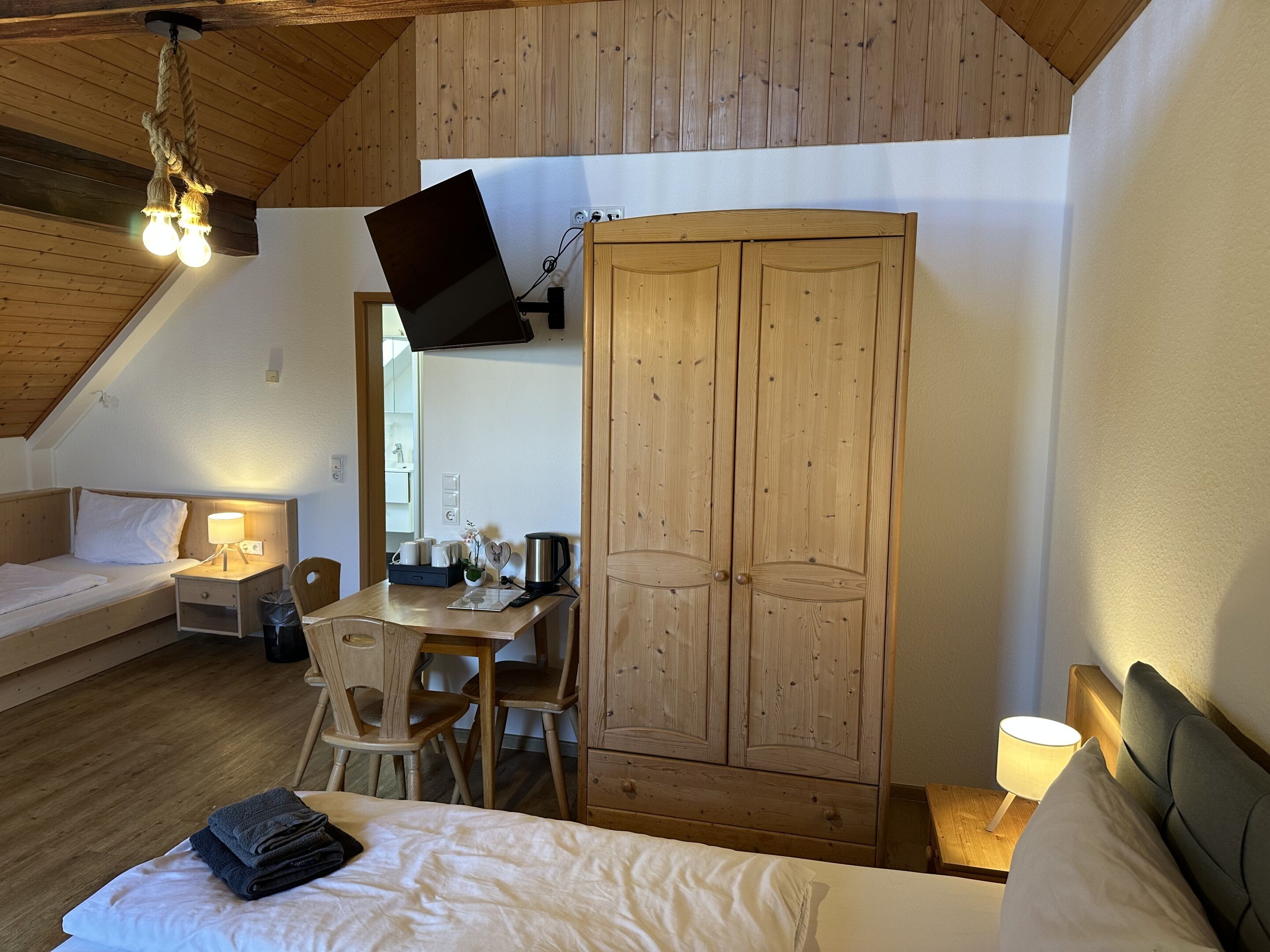 A cozy room with a bed, a desk, a wardrobe, and a TV mounted on the wall.
