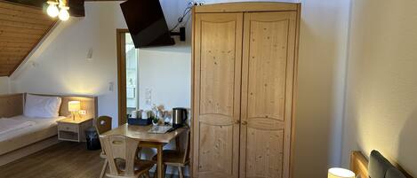 A cozy room with a bed, a desk, a wardrobe, and a TV mounted on the wall.