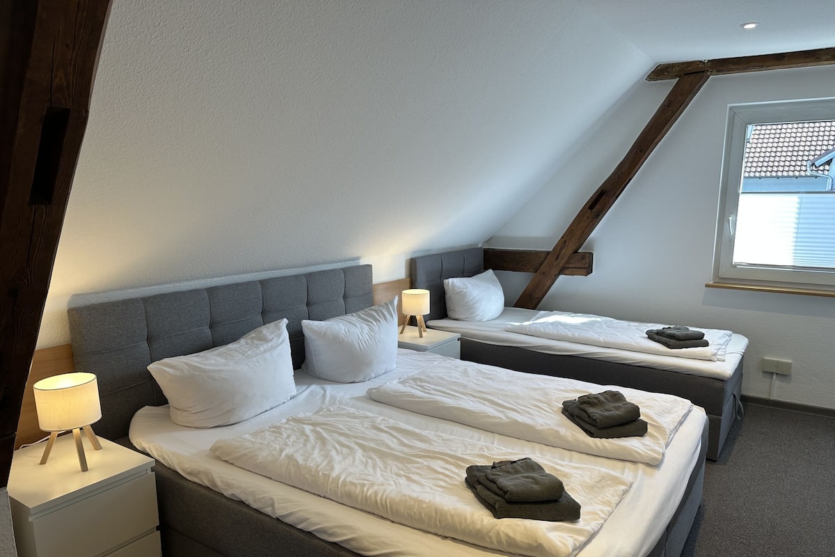 A room with two beds, a window, and a wooden beam structure.