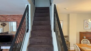 Una escalera con interior tapizado, barandillas negras y una pared de ladrillo a un lado.