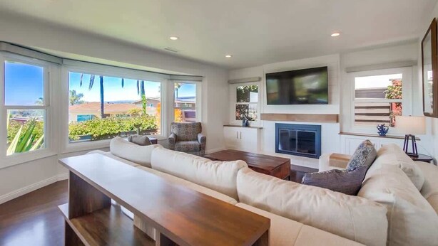 A modern living room with a sofa, a coffee table, a fireplace, and large windows.