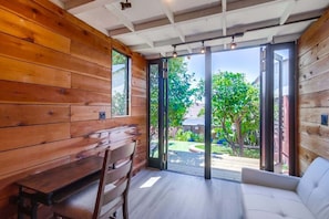 A room with wooden walls, a bench, a sofa, and a sliding glass door leading to a garden.