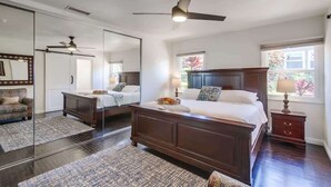 A bedroom with a large bed, a dresser, a nightstand, a mirror, and a ceiling fan.