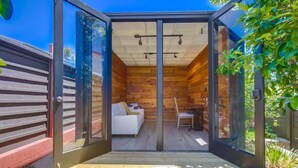 A modern, glass-enclosed room with a wooden interior, a white sofa, and a dining table.