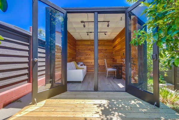 A modern, glass-enclosed room with a wooden interior, a white sofa, and a dining table.
