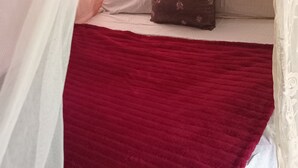 Una cama con una colcha roja, cortinas blancas y un cojín estampado.