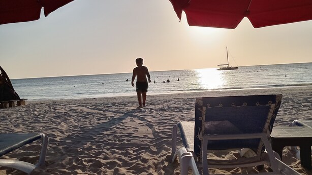 Una playa con sombrillas, sillas de descanso y una persona caminando hacia el mar.
