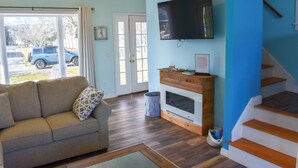 Una sala de estar con un sofá, un televisor montado en la pared, una chimenea y una escalera.