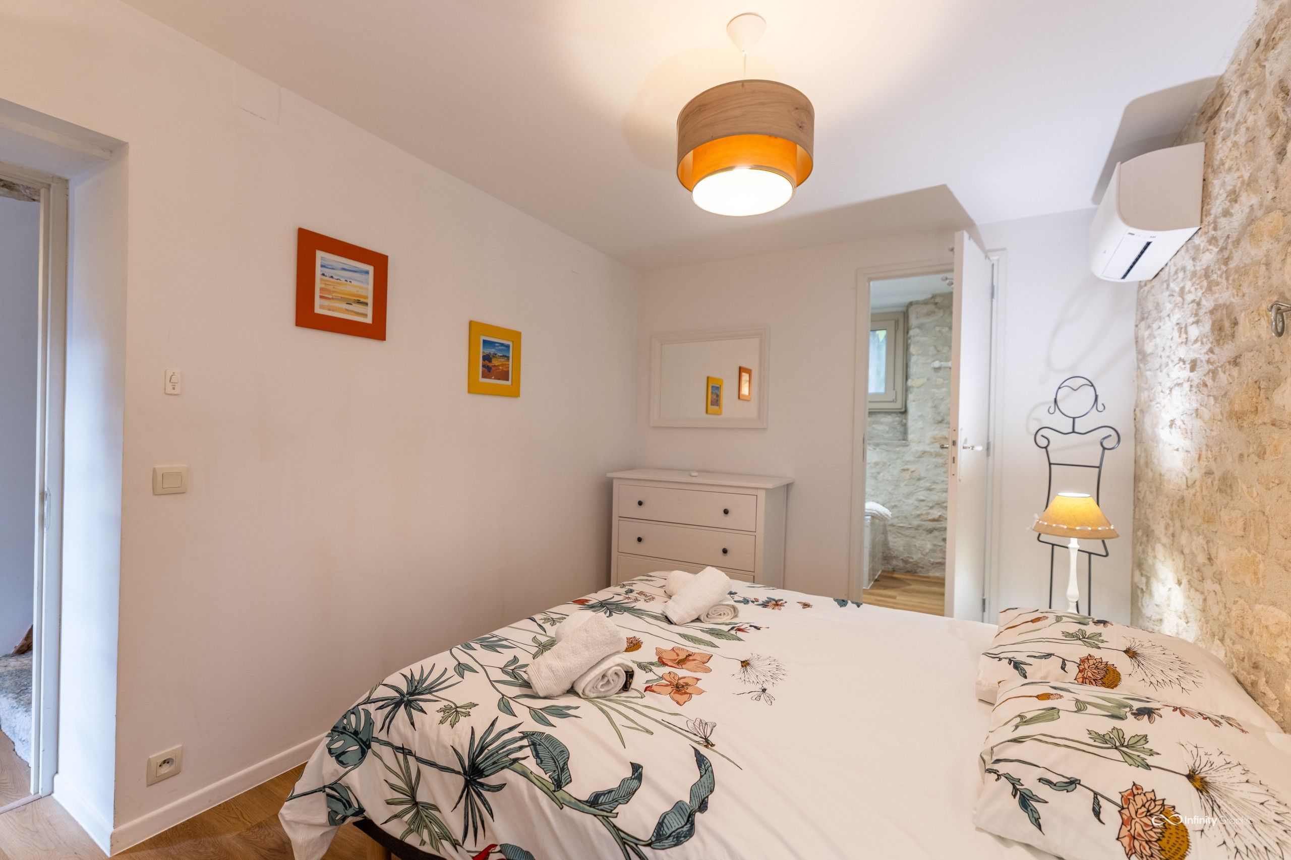 A bedroom with a bed, a dresser, a lamp, and framed pictures on the wall.