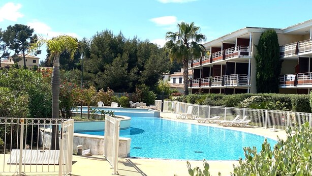 A swimming pool with a white fence, lounge chairs, and a building with balconies in the background. - "Le Paloma" swimming-pool-clim-parking (La Ciotat)