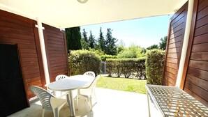A patio with a table and chairs, a metal grill, and a view of a well-maintained garden and trees. - "Le Paloma" swimming-pool-clim-parking (La Ciotat)