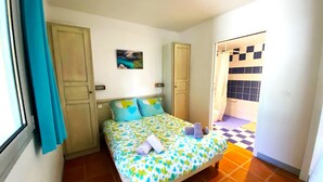 A bedroom with a bed, a bathroom visible through an open door, and a window with curtains. - "Le Paloma" swimming-pool-clim-parking (La Ciotat)