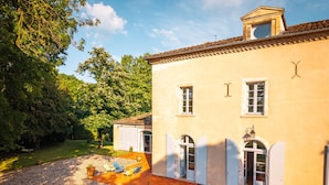 Une maison à deux étages avec un patio, un petit jardin et un grand arbre en arrière-plan.