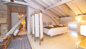 Une chambre spacieuse située dans les combles, avec un grand lit, une chaise en bois et une petite table.