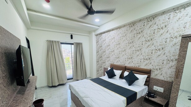 Habitación de hotel con cama, televisor, ventilador de techo, ventana con cortinas y pared con diseño.