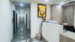 Zona de recepción de hotel con suelo de mármol, mostrador de recepción, una obra de arte enmarcada sobre el mostrador y un pasillo que conduce a otra habitación.